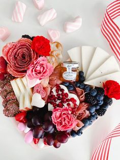 a heart shaped platter filled with cheese, fruit and flowers next to candy hearts