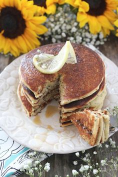 a stack of pancakes on a white plate with a slice cut out and some flowers in the background