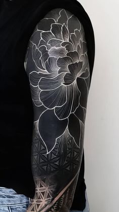 a man with a black and white flower tattoo on his arm is standing in front of a wall