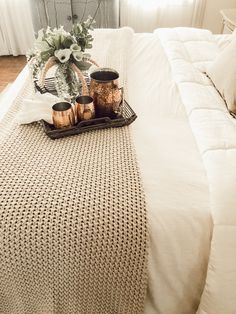 a bed with white linens and some candles on top of it, in front of a window