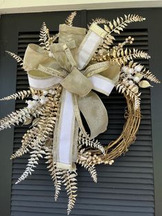 a wreath that is hanging on the side of a door with white and gold ribbons