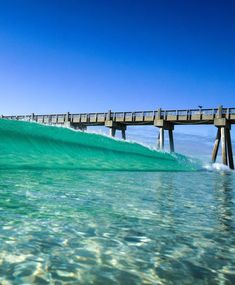 a surfer is riding the waves in front of a pier on a clear blue day