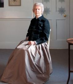 an older woman sitting in a chair wearing a long skirt