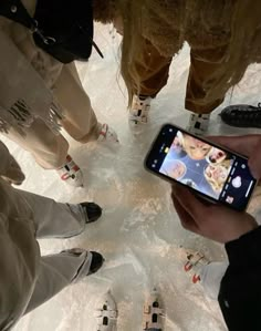 a person holding a cell phone in front of several people standing on snow covered ground