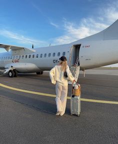 a woman in white is standing next to a luggage bag and an airplane on the tarmac