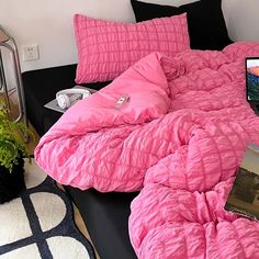 a laptop computer sitting on top of a bed covered in pink comforter and pillows