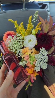 a person is holding a bottle with flowers in it on the back seat of a car