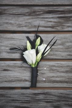 a boutonniere with white flowers and black feathers on a wooden table top