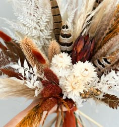 a vase filled with lots of different types of dried flowers and feathers sitting on top of a table