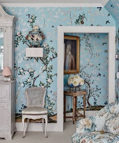 a bedroom decorated in blue and white with flowers on the wall next to a chair