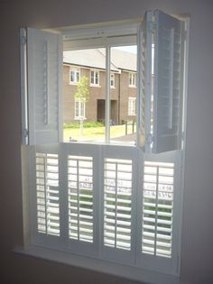 an open window with white shutters in front of a house