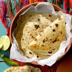 three tortillas in a bowl on a colorful table cloth with lime wedges