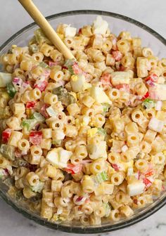 a glass bowl filled with macaroni salad and a wooden serving spoon in it