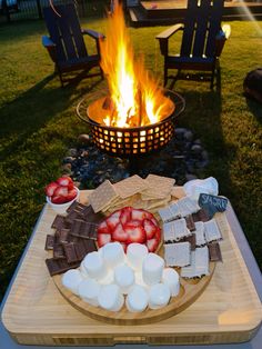 a fire pit with marshmallows, strawberries and other snacks on it