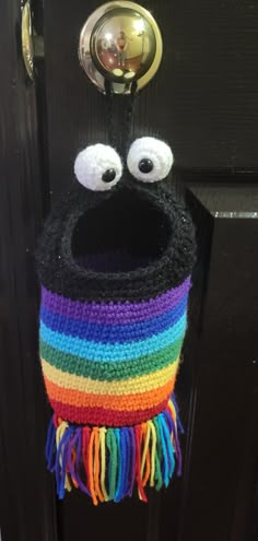 a crocheted bag with eyes and a rainbow scarf hanging from it's front door