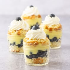 three small desserts with blueberries and whipped cream on top sit in glass containers