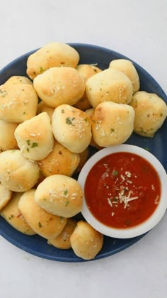 a blue plate topped with rolls covered in cheese next to a bowl of marinara sauce