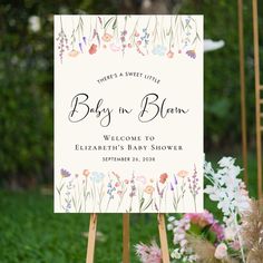 a baby in bloom welcome sign with flowers and greenery on the grass behind it