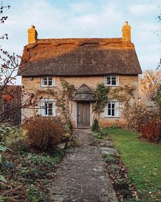 an old house with a thatched roof and stone pathway leading to the front door