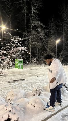 a man standing in the snow next to a tree at night with street lights behind him