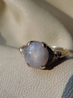 a ring with a large white stone on it's side sitting on a cloth