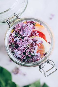 a jar filled with flowers and orange slices on top of a white table next to green leaves