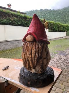 a gnome statue sitting on top of a wooden table next to a brick wall and grass covered hillside