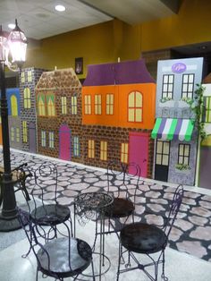 tables and chairs are arranged on the floor in front of a display of colorful houses