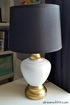 a white and gold lamp sitting on top of a table next to a book shelf