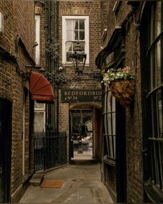 an alley way with brick buildings on both sides and flowers hanging from the windows above