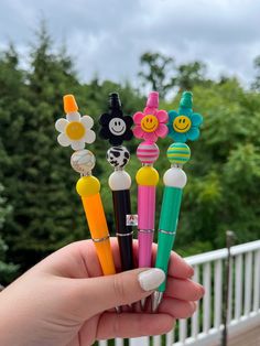 a person holding several pens with smiley faces and flowers on them in front of some trees