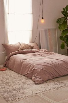 an unmade bed with pink sheets and pillows in front of a large potted plant