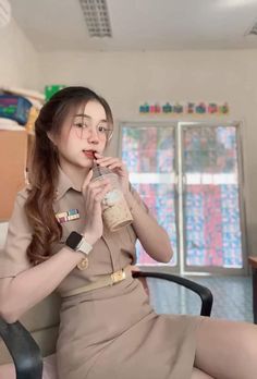 a woman in uniform sitting on a chair drinking from a bottle and looking at the camera