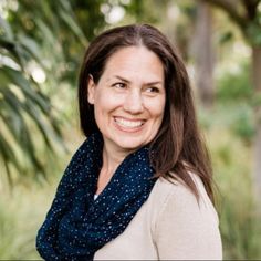 a smiling woman wearing a blue scarf in front of some trees and grass with her eyes closed