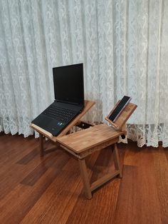 a laptop computer sitting on top of a wooden table next to a window with white curtains