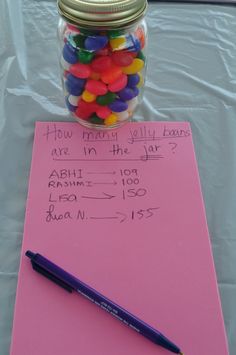 a jar filled with candy sitting on top of a pink sheet of paper next to a pen