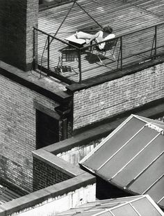 a person laying on top of a roof next to a tall brick building with a small table and chairs