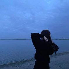 a woman is standing on the beach looking out at the water and holding her head in her hands