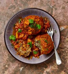 two meatballs covered in sauce and garnished with parsley on a plate