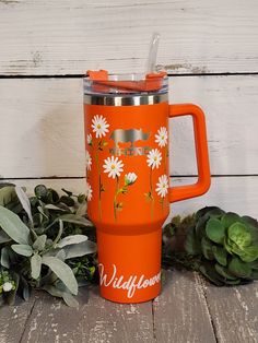 an orange travel mug with white daisies and the words wildflowers on it