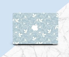 an apple laptop computer sitting on top of a white and blue marble surface with floral designs