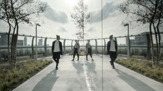 three men are walking down a walkway in front of some trees and buildings with their shadows on the ground