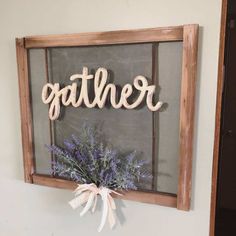 a wooden sign that says gather hanging on the side of a wall with flowers in front of it