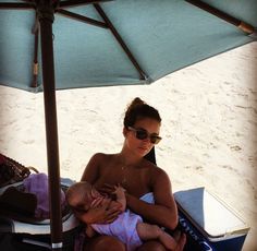 a woman holding a baby under an umbrella on the beach