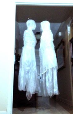 two white dresses are hanging on the wall in front of a doorway, one is wearing a veil