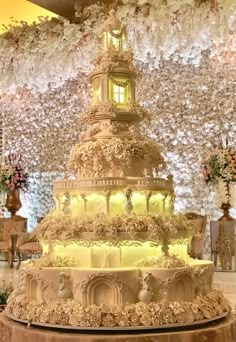 a wedding cake with white flowers on the top and sides is displayed in front of a floral wall