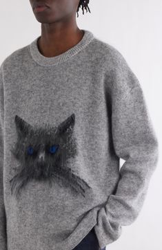 a woman wearing a grey sweater with a black cat on the front and blue eyes