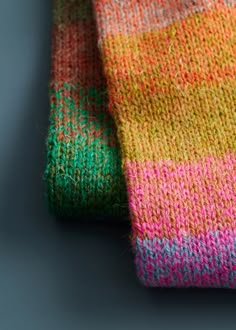 a multicolored knitted tie laying on top of a gray surface next to it