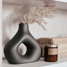 a black vase sitting on top of a white shelf next to a candle and basket