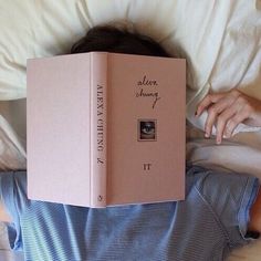 a person laying in bed with a pink book over their head and the cover is open